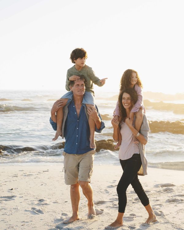 Family enjoying a beach outing at sunset with children on their shoulders
